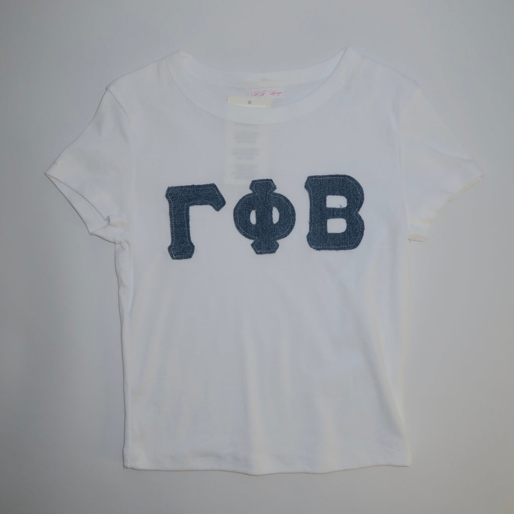 A white cotton baby tee with denim blue greek letters 'Gamma Phi Beta' printed on the front.